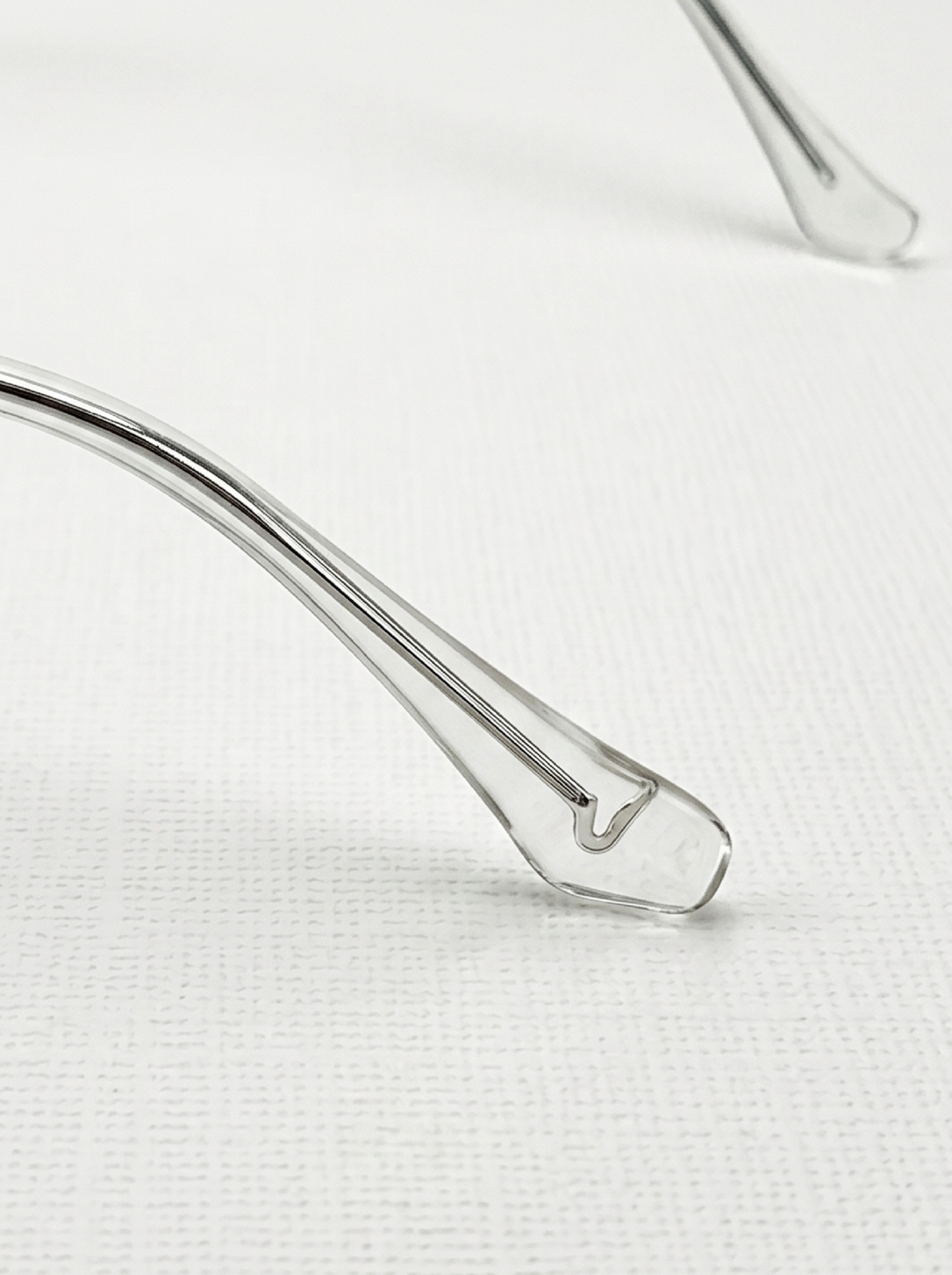 Close-up shot of transparent acetate temple on silver oversized square glasses, sleek thin metal frame texture minimalist eyewear detail photography clean neutral background