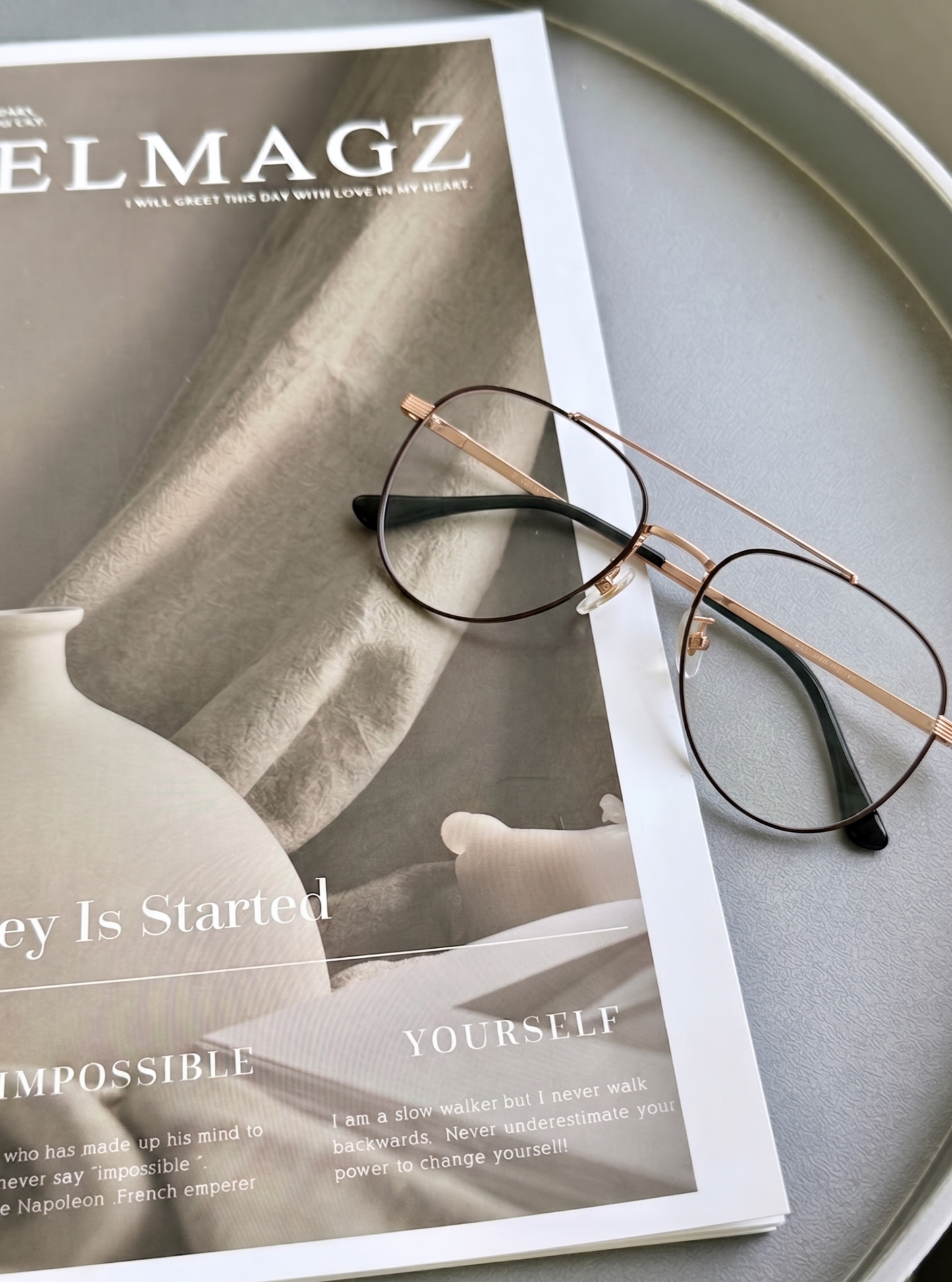 Two-tone metal clear lens glasses fashion flat lay on fashion magazine, neutral minimalist table styling retro aviator clear lens metal frame trendy daily eyewear